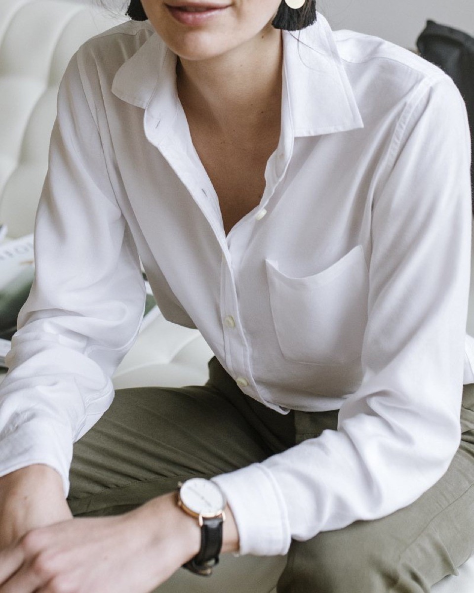 A woman in a white button-up shirt and olive trousers, seated